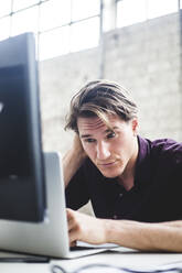 Young male entrepreneur working on start-up project while coding at desk in office - MASF13321