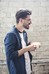 Side view of bearded smiling computer programmer holding coffee cup while standing in office - MASF13354
