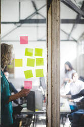 Businesswoman giving presentation to IT professionals seen through glass wall in creative office - MASF13399