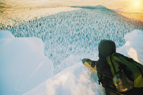 Wanderer bewundert die Aussicht von einer verschneiten Bergkuppe, lizenzfreies Stockfoto