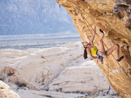 Gemischtrassiges Mädchen beim Klettern am Felsen - BLEF09956