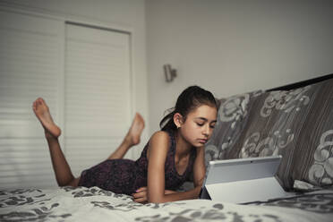 Gemischtrassiges Mädchen benutzt digitales Tablet auf dem Bett - BLEF09972