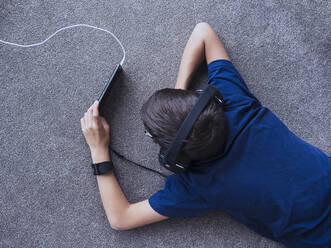 Gemischtrassiger Junge benutzt Mobiltelefon auf dem Boden - BLEF09973