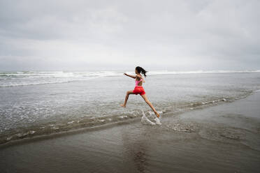 Mixed race girl running into ocean on beach - BLEF09980