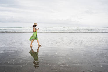 Gemischtrassige Frau geht am Strand mit Handy - BLEF09981