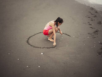 Mixed race girl drawing in beach sand - BLEF09983