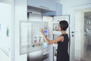 Mixed race girl using hologram refrigerator touch screen in kitchen - BLEF09988
