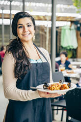 Mixed race waitress holding plate of seafood and pasta - BLEF10012