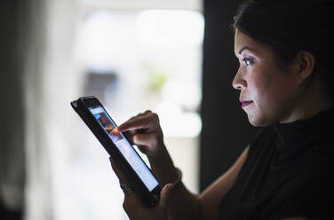 Mixed race woman using digital tablet at night - BLEF10044