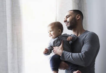 Smiling father and baby son looking out window - BLEF10053