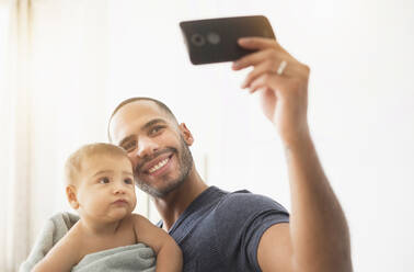 Father taking cell phone photograph with baby son - BLEF10055