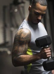 Nahaufnahme eines hispanischen Mannes, der im Fitnessstudio Gewichte hebt - BLEF10063