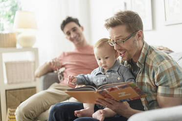 Kaukasische schwule Väter lesen ihrem Baby im Wohnzimmer vor - BLEF10091