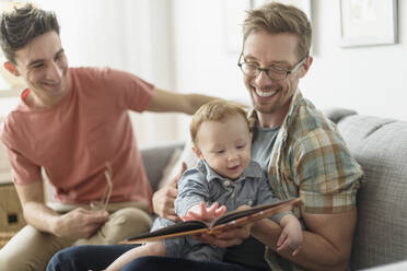 Kaukasische schwule Väter lesen ihrem Baby im Wohnzimmer vor - BLEF10092