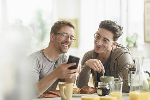 Kaukasisches schwules Paar benutzt Handy beim Frühstück - BLEF10095
