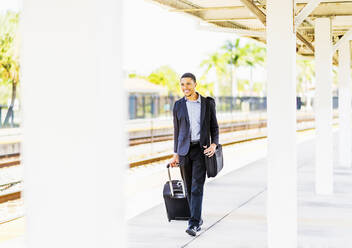 Schwarzer Geschäftsmann rollt Gepäck auf dem Bahnsteig - BLEF10138