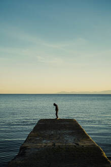 Boy in hoody standing on ocean pier, Victoria, British Columbia, Canada - FSIF04151