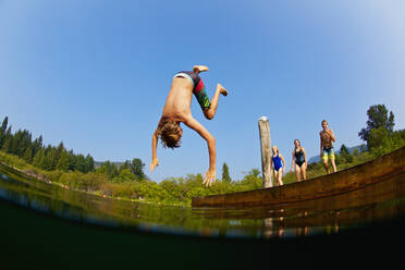 Junge, der einen Purzelbaum vom Steg in den sonnigen Sommersee macht - FSIF04160