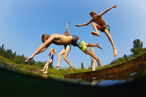 Verspielte Kinder springen vom Steg in den sonnigen Sommersee - FSIF04161
