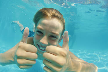 Porträt eines glücklichen, sorglosen Jungen, der im Schwimmbad unter Wasser schwimmt und den Daumen nach oben streckt - FSIF04166
