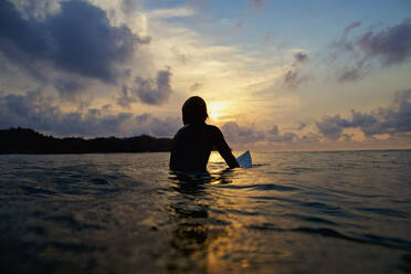 Silhouette surfer sitting on surfboard in tranquil ocean at sunset, Sayulita, Nayarit, Mexico - FSIF04185