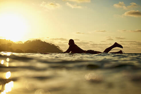 Männlicher Surfer auf dem Surfbrett auf dem sonnigen Meer bei Sonnenuntergang, Sayulita, Nayarit, Mexiko - FSIF04186