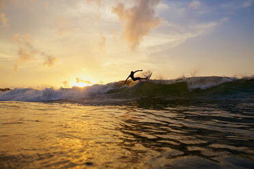 Männlicher Surfer, der bei Sonnenuntergang auf dem Meer eine Kurve von der Welle macht, Sayulita, Nayarit, Mexiko - FSIF04189