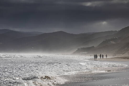 Bedrohliche Wolken über silhouettierten Menschen, die am Strand spazieren gehen, Aireys Inlet, Victoria, Australien - FSIF04242