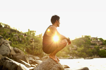 Serene young man crouching on ocean rock, Sayulita, Nayarit, Mexico - FSIF04270