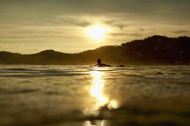 Silhouette eines jungen Mannes auf einem Surfbrett auf dem ruhigen Meer bei Sonnenuntergang, Sayulita, Nayarit, Mexiko - FSIF04273