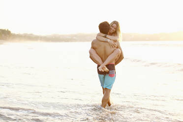 Boyfriend carrying girlfriend in ocean surf - FSIF04284