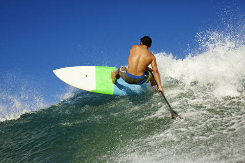 Junger, fitter Mann beim Paddeln auf einer Meereswelle, lizenzfreies Stockfoto