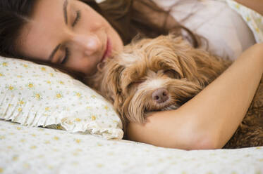Caucasian woman hugging pet dog in bed - BLEF10151