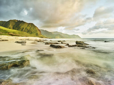 Landschaftliche Ansicht von Wellen, die am Strand im Ka'ena Point State Park gegen den Himmel plätschern, lizenzfreies Stockfoto