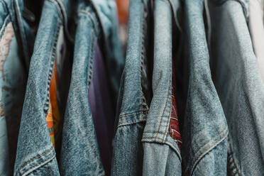 Close-up of blue denim jackets hanging on rack at clothing store - AFVF03599