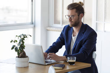 Businessman using laptop at table in modern office - JSRF00449