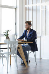 Geschäftsmann mit Laptop am Tisch in einem modernen Büro - JSRF00450