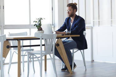 Geschäftsmann mit Laptop am Tisch in einem modernen Büro - JSRF00451