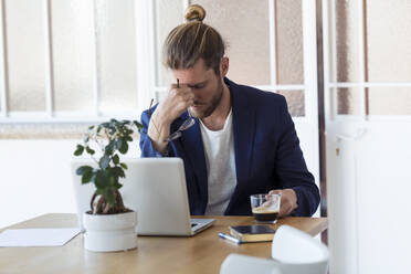 Müder Geschäftsmann sitzt am Tisch im Büro - JSRF00459