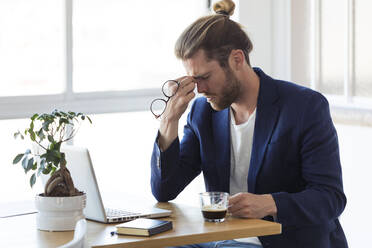 Tired businessman sitting at table in office - JSRF00460