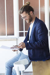 Smiling young businessman using smartphone in office - JSRF00466