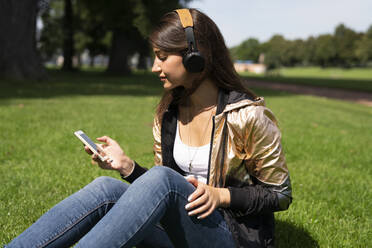 Porträt einer jungen Frau mit glänzender Jacke, die ein Smartphone und Kopfhörer benutzt - TWOF00010