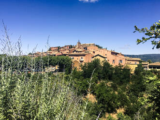 Buildings in town amidst plants and trees against blue sky on sunny day - SBDF04009