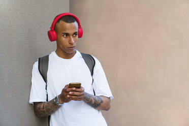 Portrait of tattooed young man listening music with smartphone and red headphones - MGIF00554