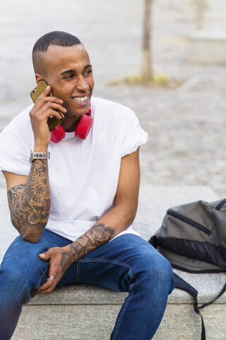 Porträt eines tätowierten jungen Mannes, der auf einer Bank sitzt und telefoniert, lizenzfreies Stockfoto