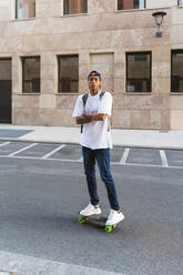 Porträt eines tätowierten jungen Mannes auf einem Skateboard - MGIF00572
