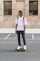 Tattooed young man standing on skateboard looking at distance - MGIF00575