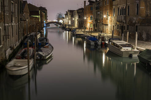 Boote im Kanal inmitten von Gebäuden in Venedig bei Nacht - LJF00461