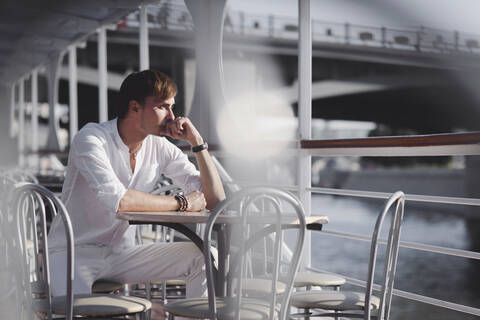 Nachdenklicher Mann in weißer Kleidung, der auf einem Ausflugsboot sitzt und bei Sonnenlicht in die Ferne schaut, Moskau, Russland, lizenzfreies Stockfoto