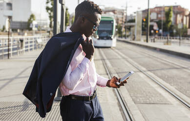 Junger Geschäftsmann benutzt sein Smartphone und wartet auf die Straßenbahn - LJF00463